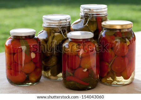 Glass jars of homemade canned tomatoes and cucumbers on the outdoors ...