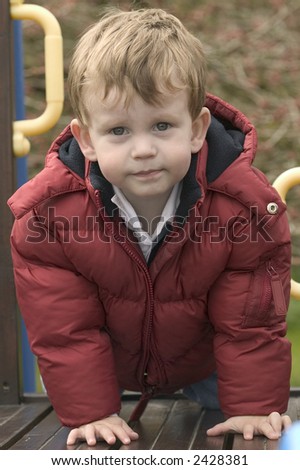 A young boy wearing a warm coat on a garden climbing frame.