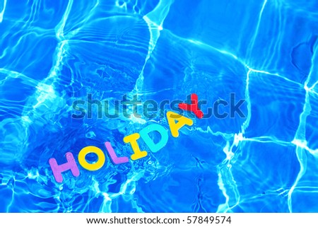 The word HOLIDAY made from foam letters floating on the water surface of a swimming pool