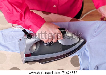 Photo of a woman ironing a work shirt with a steam iron.