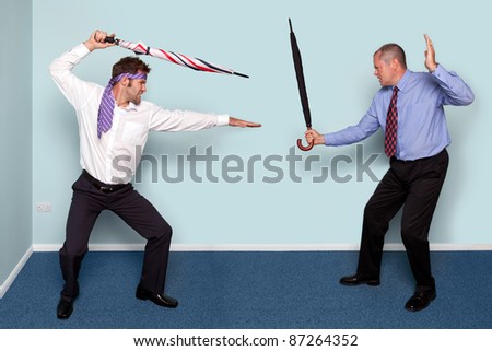 Photo of two businessmen having a sword fight using umbrellas, good image to convey conflict, rivalry or disagreement.