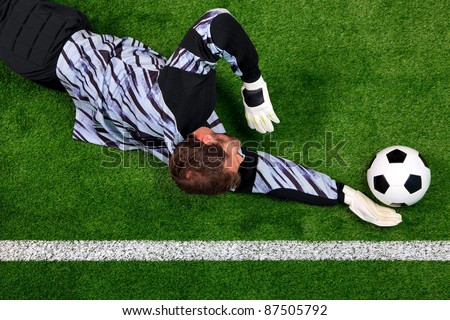Overhead photo of a football goalkeeper diving to save the ball from crossing the goal line.