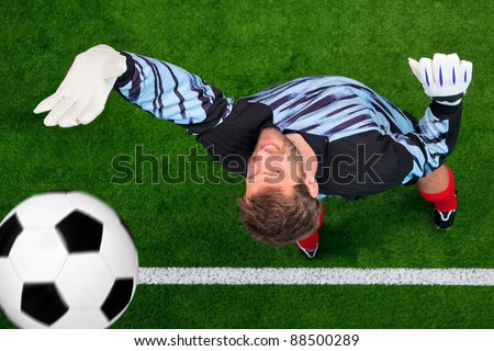 Overhead photo of a football goalkeeper missing saving the ball as it crosses over the line. Slight motion blur on the ball, focus is on his face.
