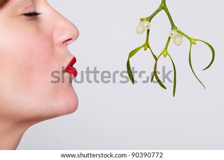 Photo of a woman with her eyes closed and red lipstick on waiting to be kissed under the mistletoe.
