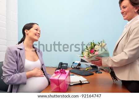 Photo of a pregnant office worker being given a gift and flowers by a colleague as she goes on maternity leave.