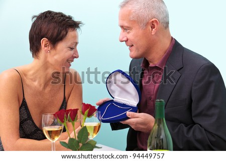 Photo of a mature man giving his wife a diamond necklace whilst sat at a table in a restaurant.