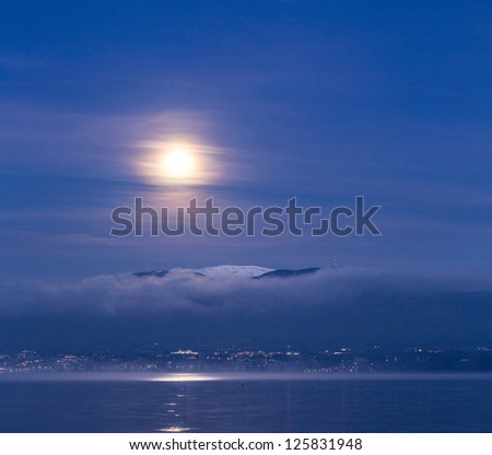 Full moon over Jura mountain range and Lake Geneva in a winter dawn
