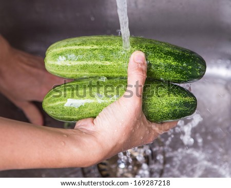 Female hands washing cucumber at the kitchen sink