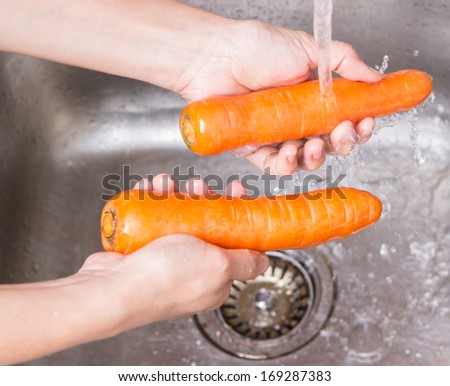 Female hands washing carrot vegetable at the kitchen sink