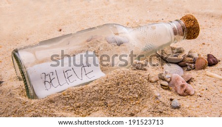 Concept image of BELIEVE message written on a piece of paper in a glass bottle on beach sand