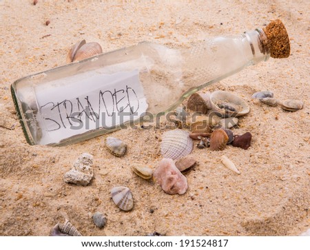 Concept image of word STRANDED message in a glass bottle on beach sand