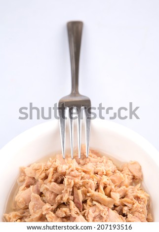 Flaked pieces of tuna in white bowl with a fork