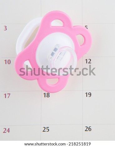 Concept image of baby girl pregnancy delivery due date with calendar page and pink  pacifier.