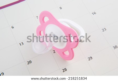 Concept image of baby girl pregnancy delivery due date with calendar page and pink pacifier.