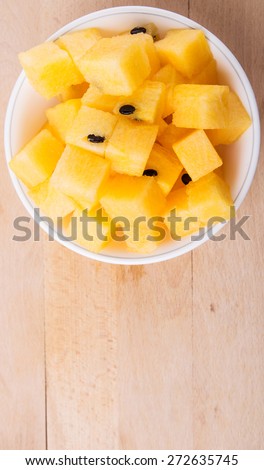 Bite size yellow watermelon fruit in white bowl on wooden cutting board