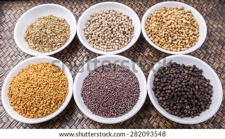 Coriander seed, fenugreek seed, black pepper, white pepper, black mustard seed and cumin seed in white container on wicker surface