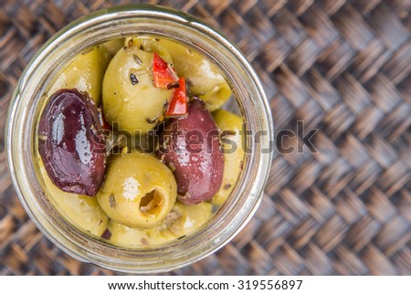 Pickled olive in a mason jar over wicker background