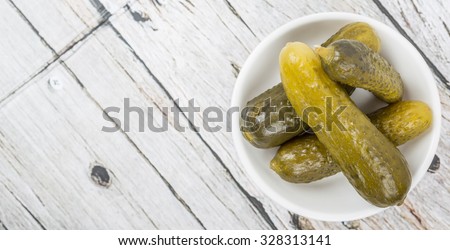 Dill pickles in a white bowl over wooden background
