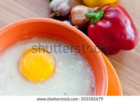 Rice porridge with egg in orange bowl on wood table with paprika and garlic.