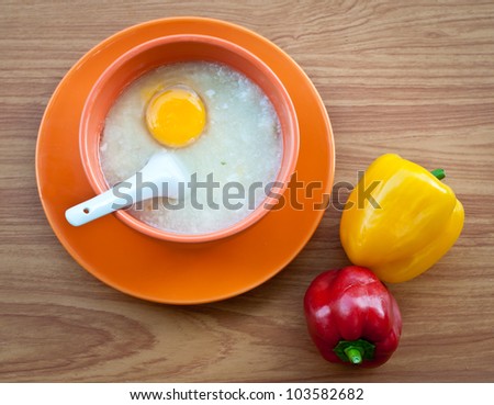Rice porridge with egg in orange bowl on wood table with paprika .