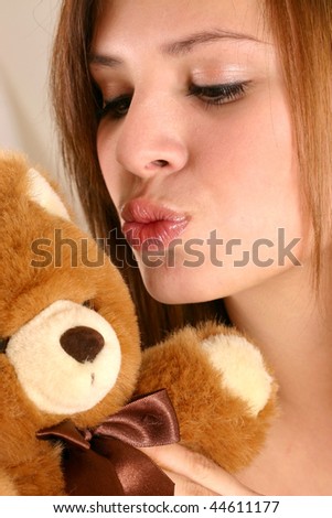 Macro view of a young woman or teenage girl cuddling a stuffed toy bear showing face lips hands before a white background