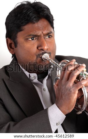 Indian man with dark skin hair beard and mustache wearing a jacket and playing a silver trumpet before a white background
