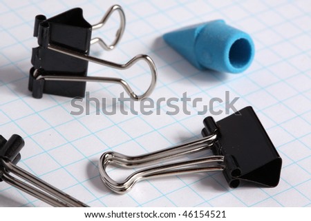Macro view of metal binder clips and blue pencil eraser on white grid paper