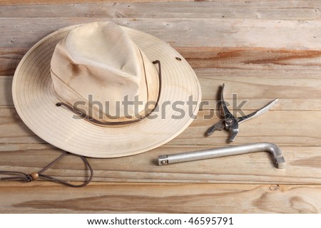 Old cloth work hat with a leather strap with wrench handle and slip joint pliers on a weathered wooden plank deck