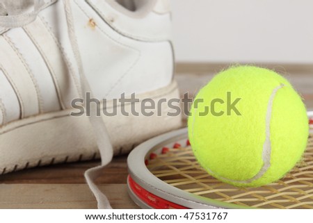 Yellow tennis ball and old white tennis shoe with aluminum racket on a weathered  wooden plank deck
