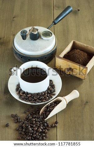 cup of coffee with bean and old coffee roaster, wooden table
