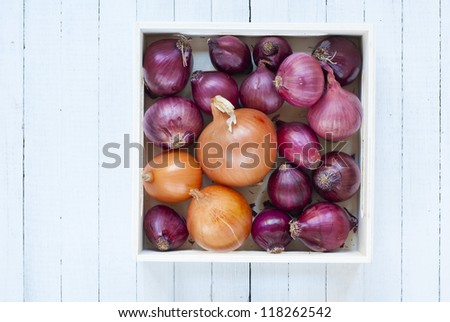 onions in wooden tray, white wood table background, top view