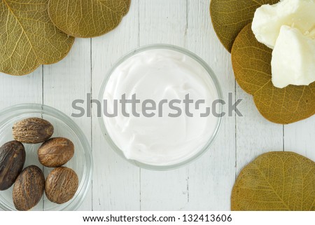 organic moisturizer creme, shea butter and shea butter nuts on white wood
