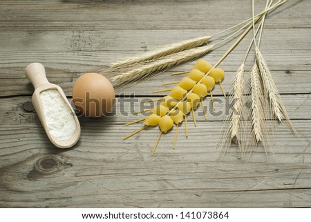 wheat ears, egg and flour on wooden spoon, wood table