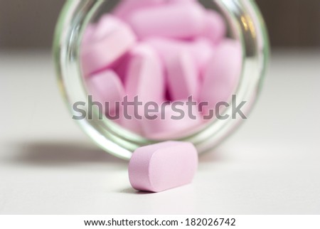 pink vitamin pills in glass jar, on white table
