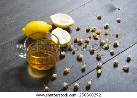 cup of chamomile tea with dried flowers and lemons on black wood table