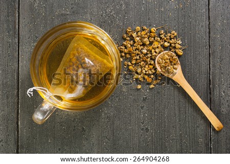 cup of chamomile tea with different size dried flowers on black wood table