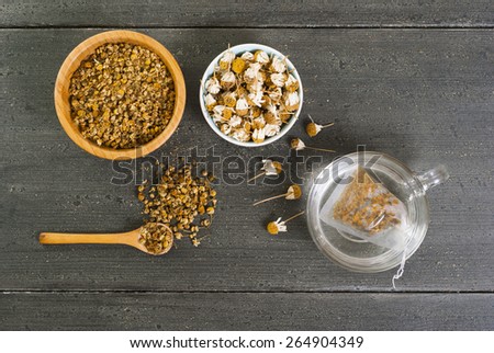cup of chamomile tea with different size dried flowers on black wood table