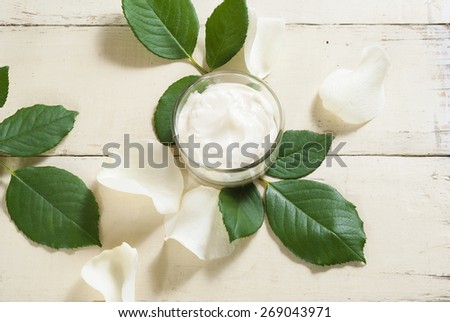 cosmetic cream with white rose petals on bright wooden table
