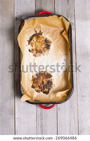 burned food prints on baking paper, old enamel frying pan on wooden table