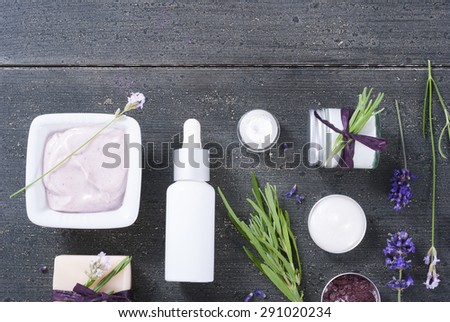 different cosmetic creams, bath salt, soap, anti aging serum pipette with fresh lavender flowers on black wooden texture