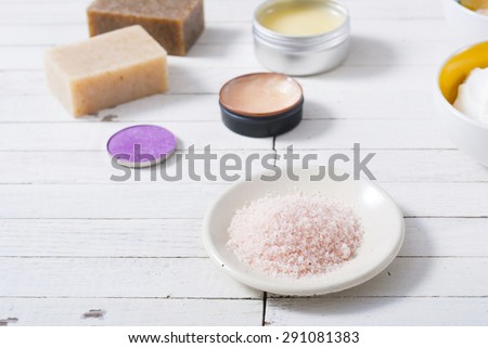 different bath salts, bees wax , makeup base, powder compact, soaps and cosmetic creams on white wooden background