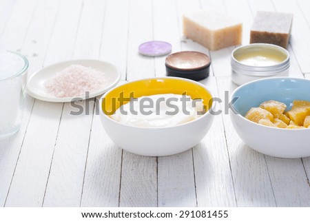 different bath salts, bees wax , makeup base, soaps and cosmetic creams on white wooden background