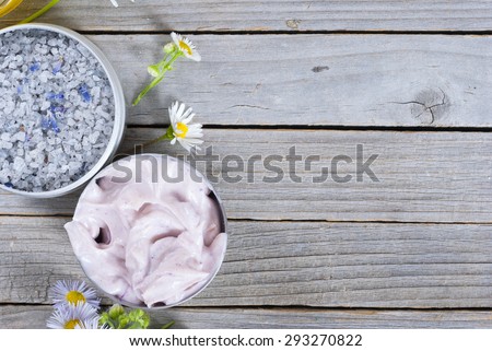 pink moisturizer cream, blue bath salt and white flowers on natural rusty wood table