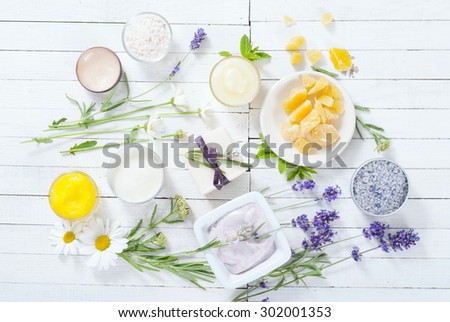 cosmetic creams, lip balm, soap and bath salt with herbal flowers on white wooden table