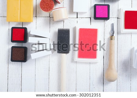 handicraft equipments, ink pads, lino cutter, paint roller and plasticine blocks on white wood table