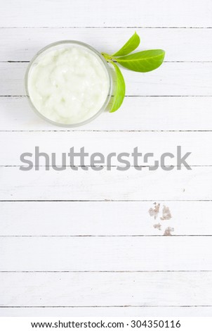cosmetic cream in glass pot and leaves on white wood