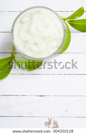 cosmetic cream in glass pot and leaves on white wood