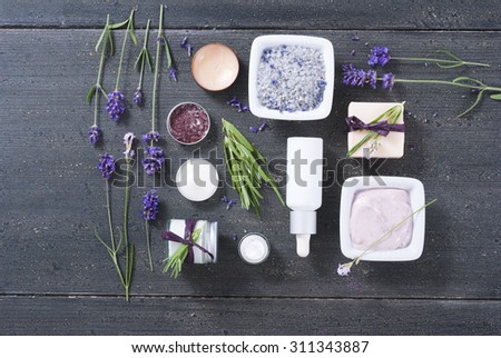 different cosmetic creams, bath salt, soap, anti aging serum pipette with fresh lavender flowers on black wooden texture