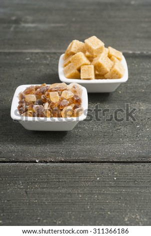 brown cubes and rock sugar on white square dishes, dark wood table
