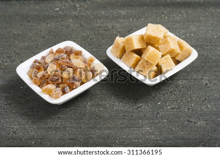 brown cubes and rock sugar on white square dishes, dark wood table